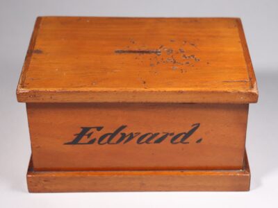 a wood money box with 'Edward' written on the front in black paint.