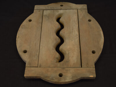 Round wooden block with holes around edge and wave shaped cut out in centre